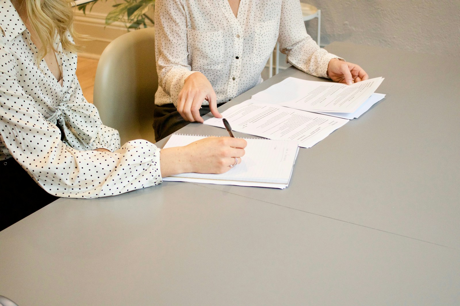 woman signing on white printer paper beside woman about to touch the documents, business