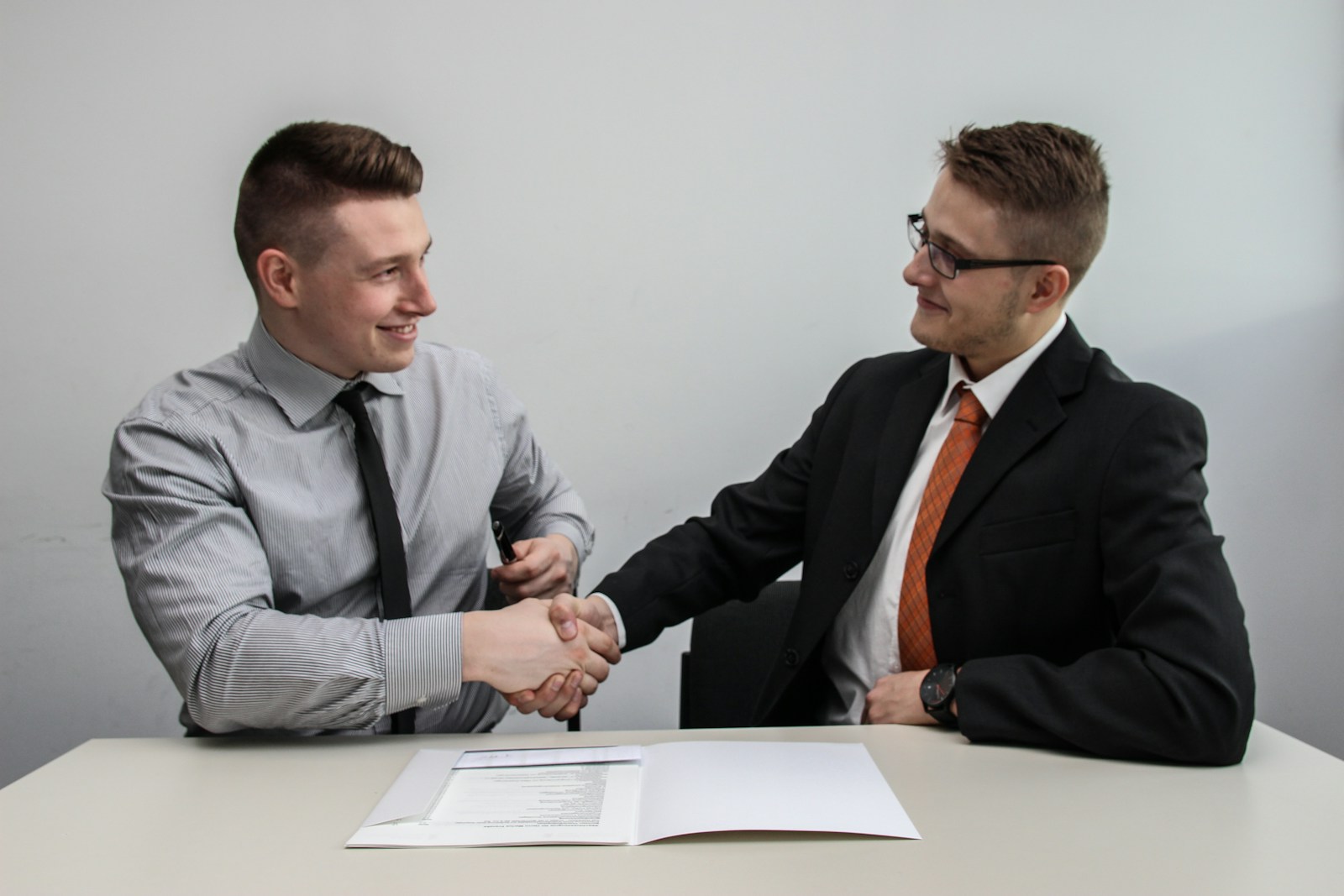 two men facing each other while shake hands and smiling, business